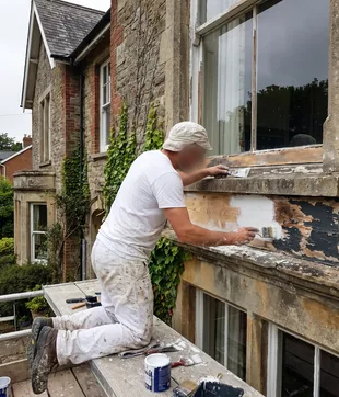 Schilder herstelt en grondt de verweerde onderdorpel van een hoog raam