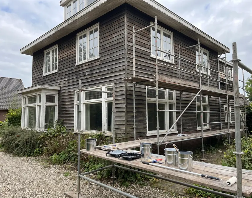 Geschilderde houten gevelbekleding en witte kozijnen van een villa met steiger ervoor