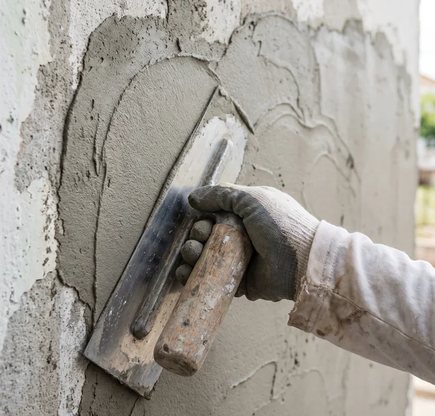 Handen met een stalen spaan die glad stucwerk op een wand aanbrengt