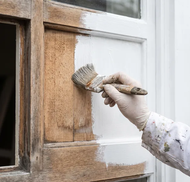 Kwast brengt witte grondverf aan op kaal geschuurd hout van een kozijn