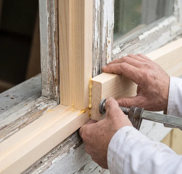 Handen zetten een nieuw stuk hout in een gerepareerd houten kozijn